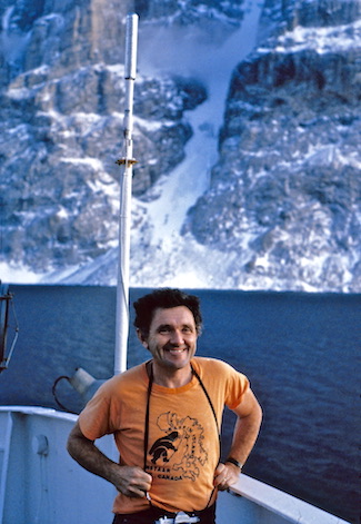 John poses near the bow of a ship overlooking a steep fjord